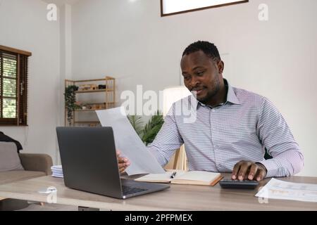 Focused african businessman holding documents looking at laptop doing research. business financial analyst concept Stock Photo