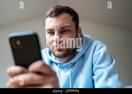 Man in earphones and blue hoodie using his cell phone. Stock Photo