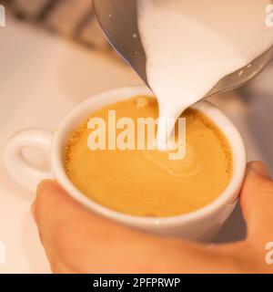 Caucasian bartender prepares coffee while pouring milk into white cup Stock Photo