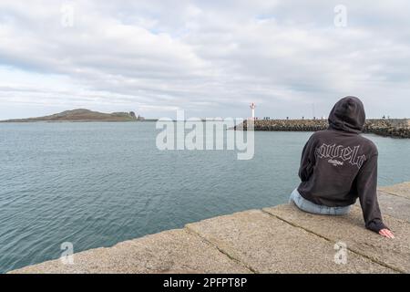 Person looking at the Howth Lighthouse on the East Pier from the West Pier with Ireland's Eye island in the distance, Howth, Dublin, Ireland Stock Photo