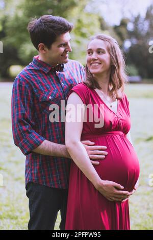 Young married couple expecting a baby soon, wife in last trimester. They are out in the park. Stock Photo
