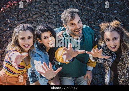 An overhead shot captures a happy group of four young adults, one man and three women, dressed in nostalgic 90s style outfits, smiling and looking at Stock Photo