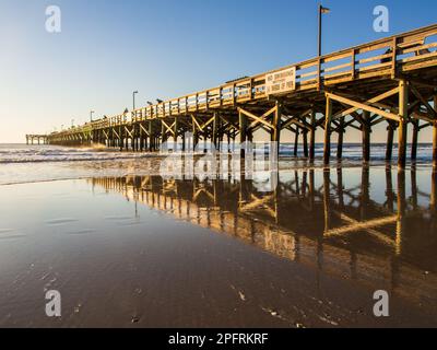 Long wooden pier on the Atlantic coast with setting sun reflecting in the shallow water on the beach. Stock Photo