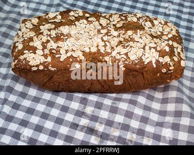 Home made baked bread with oats on top on a checkered linen cloth. Stock Photo