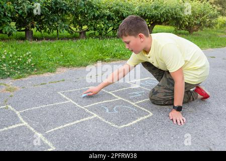 The boy draws on the pavement with crayons in the park Stock Photo