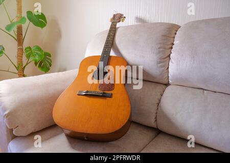Old acoustic guitar lying on the sofa in the living room Stock Photo