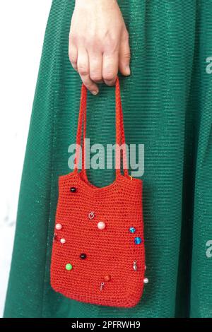 A red purse bag knitted with rhinestones in female hands against the background of a green dress. Stock Photo