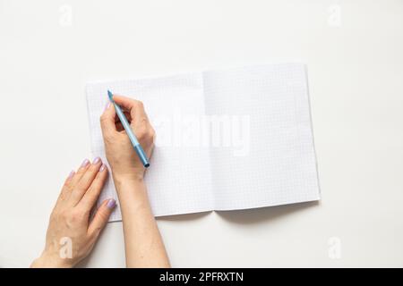 Female hands write in a notebook in a cage on a white background, blank pages Stock Photo