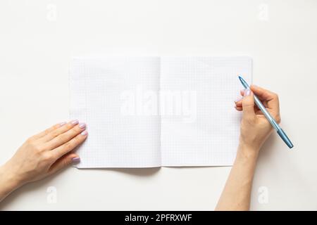 Female hands write in a notebook in a cage on a white background, blank pages Stock Photo