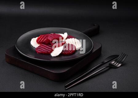 Delicious fresh mozzarella and boiled beets cut into slices on a round ceramic plate on a dark concrete background Stock Photo