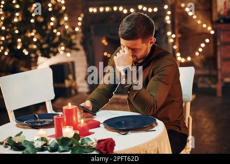 Young handsome man sits by the table and waits for girlfriend for romantic dinner in restaurant Stock Photo