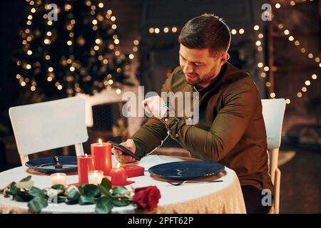 Young handsome man sits by the table and waits for girlfriend for romantic dinner in restaurant Stock Photo