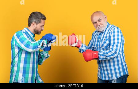 aggressive generation men fighting on background. photo of generation men fighting wear boxing gloves. two generation men fighting isolated on yellow. Stock Photo