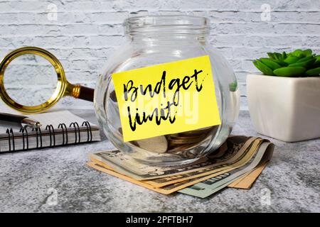 A tablet with the text BUDGET LIMIT on white paper, a magnifier, glasses, golden paper clips and a pen lie on a white office table. Top view, flat lay Stock Photo