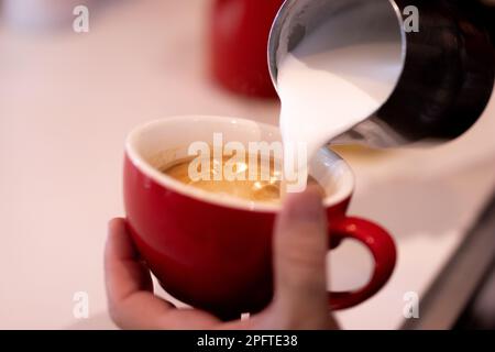 Caucasian bartender prepares coffee while pouring milk into red cup Stock Photo