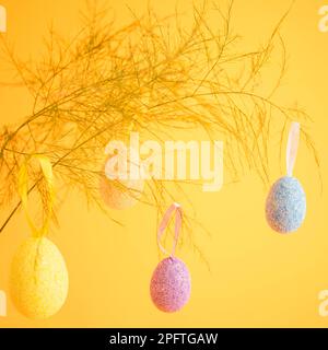 Multicolor easter eggs hanging of the branch, placed on a bright yellow background Stock Photo
