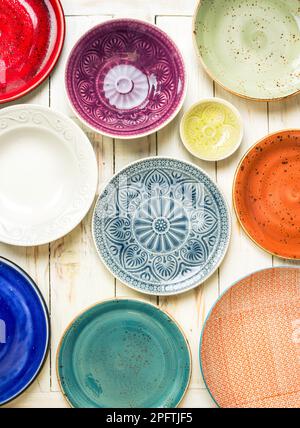 Different antique vintage multicolored empty plates and bowls on a white old wooden table. Table setting. Shabby chic/retro style. Top view. Stock Photo