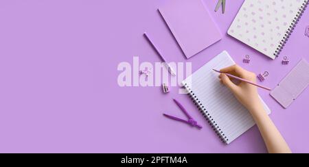 Female hand with notebooks and stationery on lilac background with space for text Stock Photo