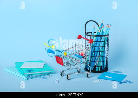 Shopping cart with stationery on blue background Stock Photo