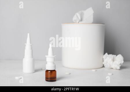 Bottles of drops with pills and tissue box on table near grey wall. Allergy concept Stock Photo