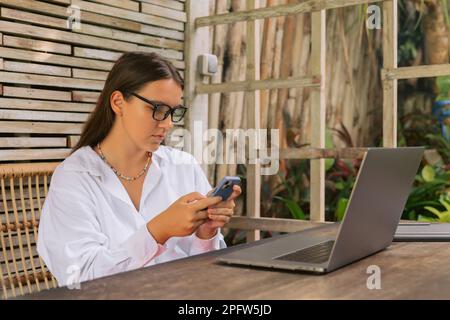 Freelancer woman using smartphone and laptop computer in summer cafe Stock Photo