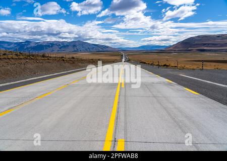 A long straight road with yellow lines leading towards mountains that crosses the Atacama desert in Chile. Dark clouds. Stock Photo