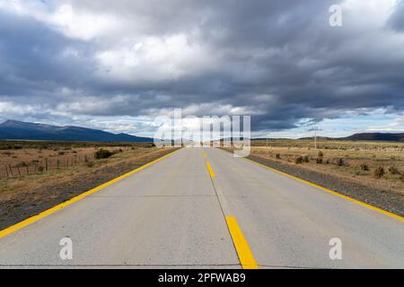 A long straight road with yellow lines leading towards mountains that crosses the Atacama desert in Chile. Sun with clouds in the blue sky. Stock Photo