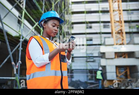 Managing a construction project with the ease of mobile technology. a young woman using a smartphone while working at a construction site. Stock Photo