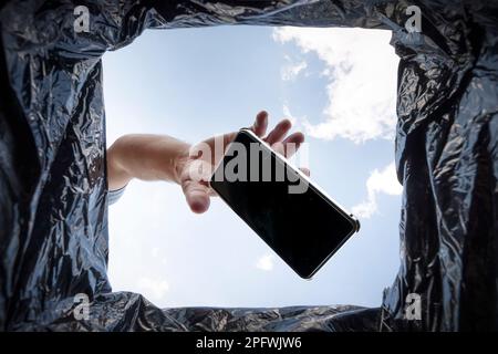 a man throws a non-working smartphone into a trash can. Bottom view from the trash can. The problem of recycling and pollution of the planet with garb Stock Photo