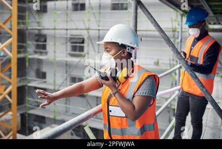 Shes just raised the bar in urban development. a young woman using a walkie talkie while working with her colleague at a construction site. Stock Photo