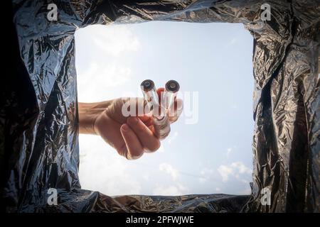 Disposal of batteries. A man puts old used AA batteries in a trash can. Bottom view. Stock Photo