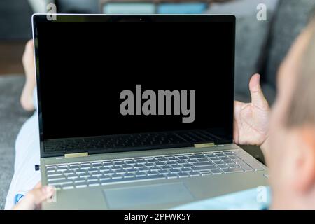 The man is lying on the sofa and looking at the empty black laptop screen. Copy space. The space is empty for text and design Stock Photo