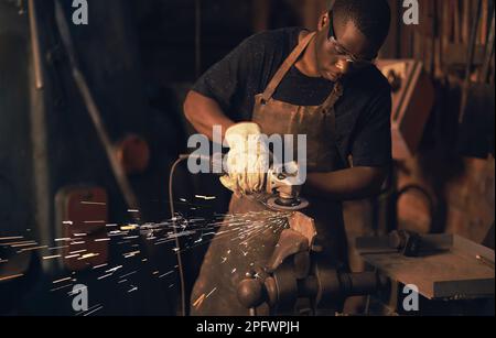 Sparks fly in the heat of the moment. a young man using an angle grinder while working at a foundry. Stock Photo