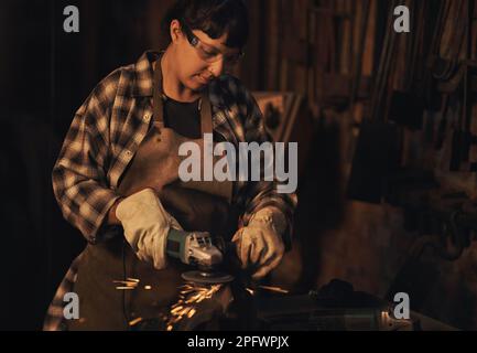 Breaking new ground with her brand of work. a young woman using an angle grinder while working at a foundry. Stock Photo