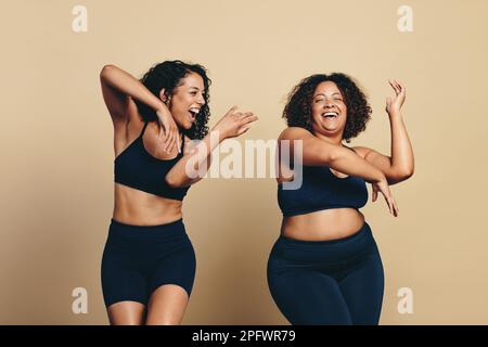 Two young women, wearing sports clothing and full of vitality, dance and exercise together in a studio. Happy female athletes having fun and celebrati Stock Photo