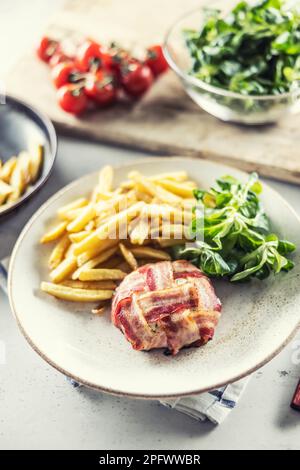 Round cheese wrap in prosciutto served with fries, salad and cherry tomatoes. Stock Photo