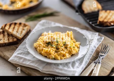Smooth scrambled eggs and crunchy toasts served in a plate with cutlery on the side. Stock Photo
