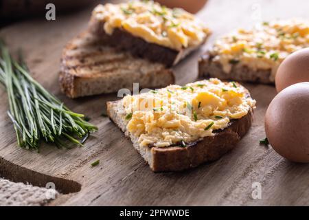 Fresh scrambled eggs spread on a slice of bread with whole eggs and fresh chive on the side. Stock Photo