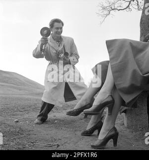 Professional photographer in the 1950s. Erich Conard, born 1924 with his Hasselblad camera and flash equipment ready to use. By the looks of the two pair of womens legs, some kind of fashion photography is going on.   Sweden in July 1952 Conard ref 2003 Stock Photo