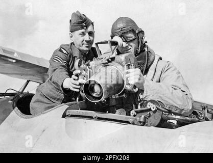 In the 1930s. A crewmember of a military airplane with a soldier at a camera mounted on the airplane. The camera might be new and some guidence in how to operate it is needed. The man dressed in a flying suit is using the sight and focus on something. England 1939 Stock Photo