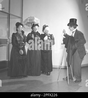 Three elderly women dressed in dresses from the turn of the century pose in front of a photographer with a camera. Sweden october 1953. Ref SSMSAX000194L Stock Photo