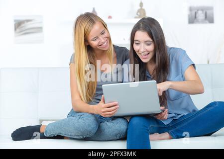 two smiling girlfriends sitting on sofa and doing homework Stock Photo