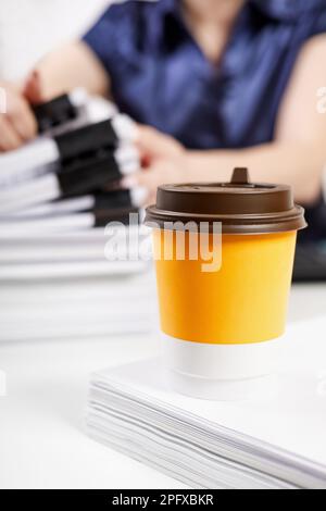 A cup of coffee on the background of an office worker sorts out a stack of papers fastened with Binder Clips Stock Photo