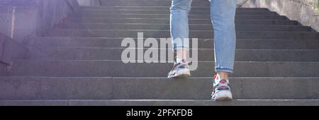 Woman in jeans going up steep stairs Stock Photo