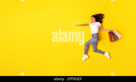 Excited Woman Carrying Shopping Bags Pointing Finger Aside, Yellow Background Stock Photo