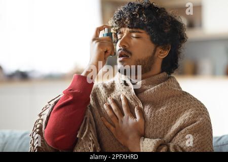Portrait of sick young indian man using inhaler at home Stock Photo