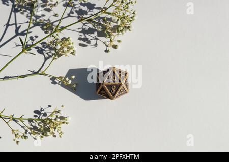 Close-up view of a single, 20-sided bronze die resting on a white paper background Stock Photo