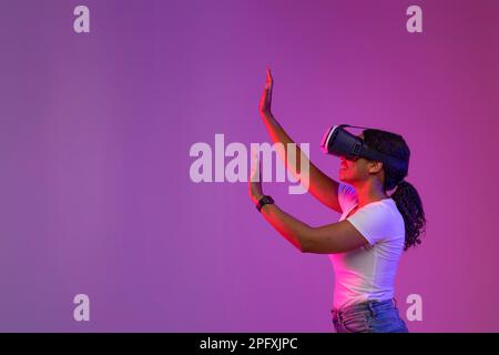 Black Female In VR Glasses Touching Imaginary Wall While Playing Video Game Stock Photo