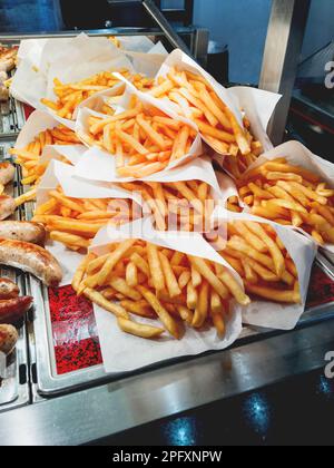 Portions of french fries in white packages lie in the shop window. Junkfood in storefront. Tasty and unhealthy fastfood. Stock Photo