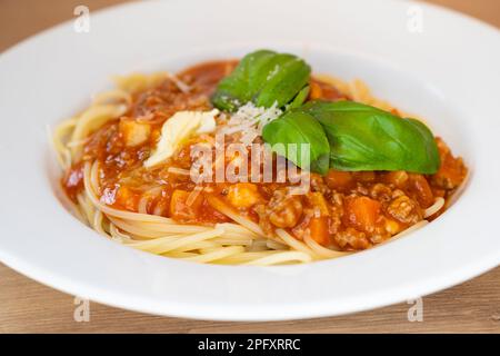homemade spaghetti bolognese with minced meat with juicy green basil, parmesan cheese, carrot pieces and butter shavings Stock Photo